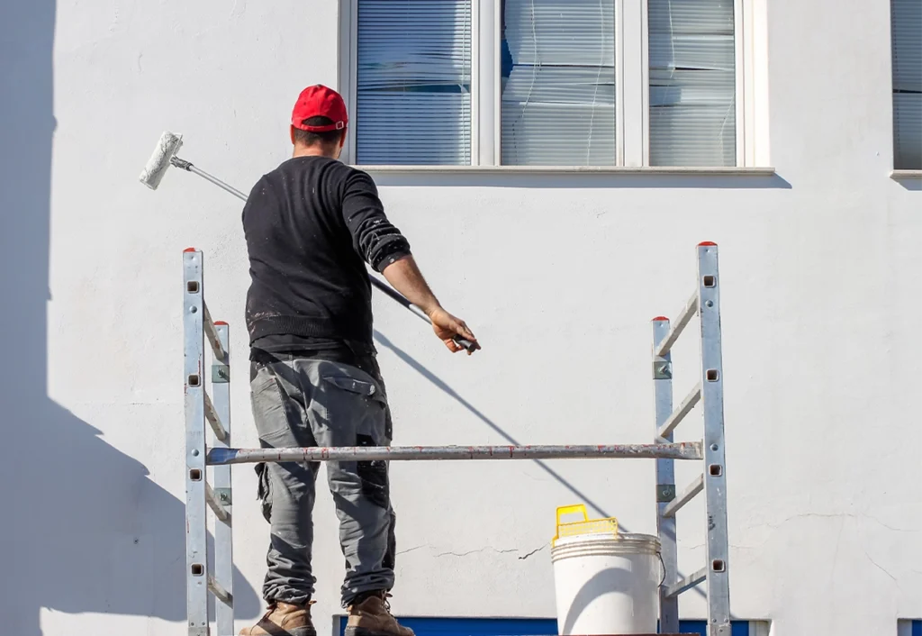 Ein Maler auf einem Gerüst streicht eine weiße Fassade.